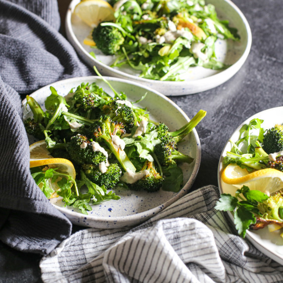 Three plates with Whole30 Broccoli Salad and herbed tahini sauce on a black countertop