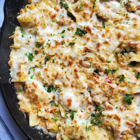 A blanket of lightly browned mozzarella on top of ravioli with the black skillet peeking out.