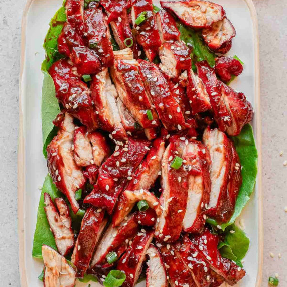 Sliced, red char siu chicken on green lettuce, garnished with sesame seeds and green onions.