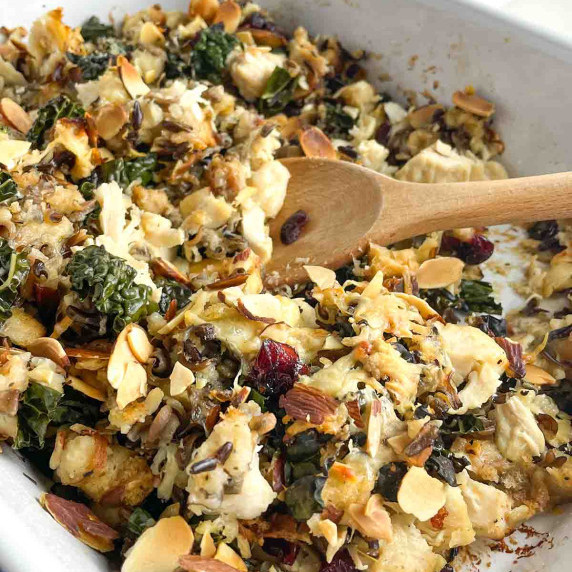 White casserole dish and white plate with chicken stuffing casserole on white countertop. 