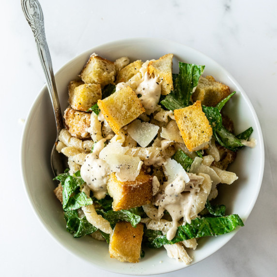 chicken caesar pasta salad in a white bowl with a fork.