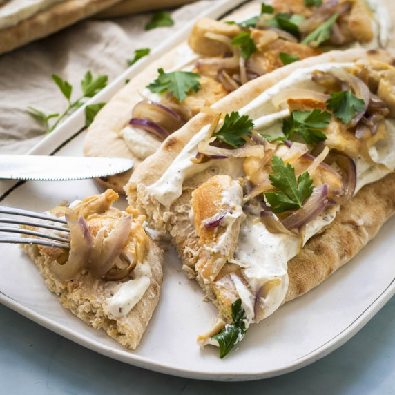 Angled side shot of two chicken pitas on a white plate with a fork taking a piece off of one pita.