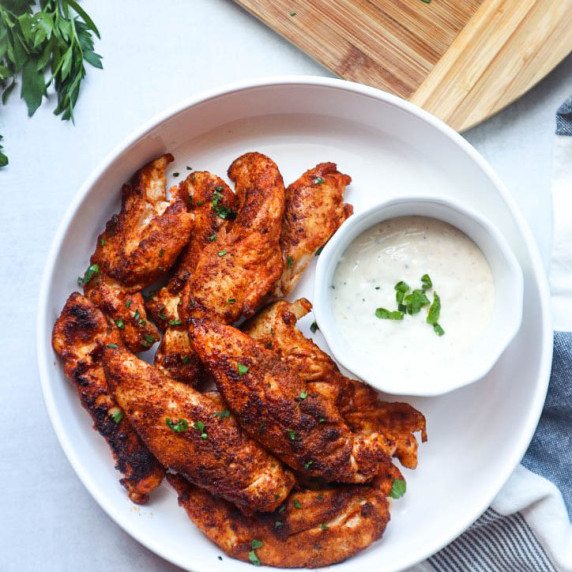 white bowl with blackened chicken tenders topped with parsley next to a small bowl with ranch 