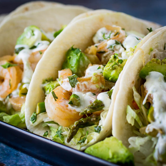 Side close up shot of shrimp tacos garnished with lime crema and herbs.