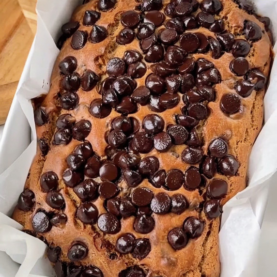 Freshly baked chocolate chip banana bread in a loaf pan, topped with sugar-free chocolate chips.