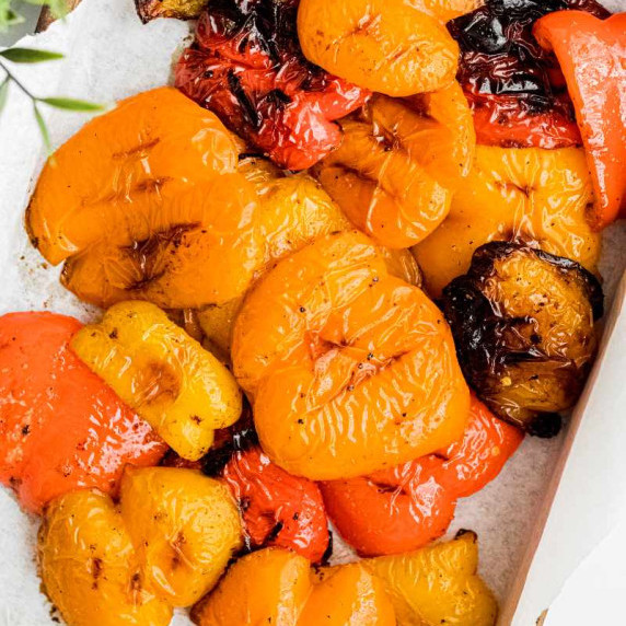 Yellow, red, and orange grilled bell pepper pieces piled on a wooden serving tray.