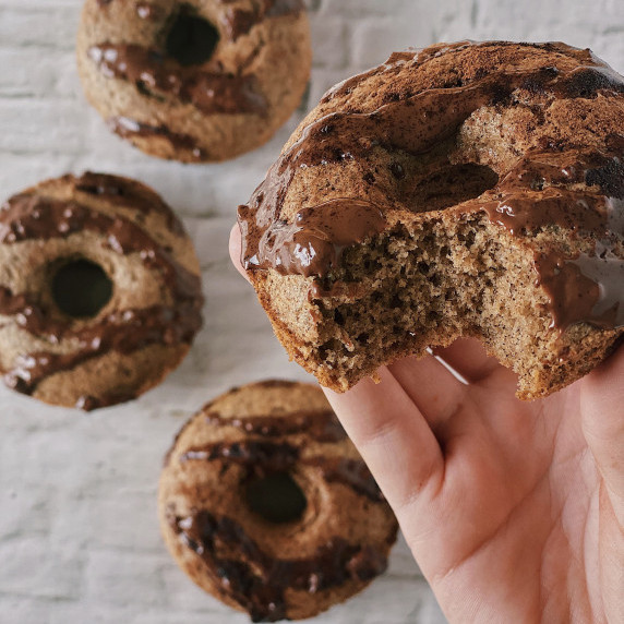 A close up of a protein donut with a bite taken out of with three other donuts in the background