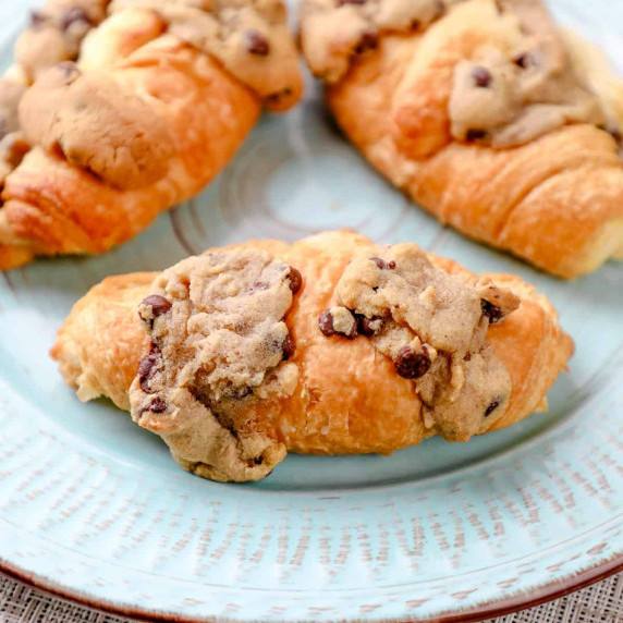 three cookie dough croissants topped with more chocolate chip cookie dough on a plate.