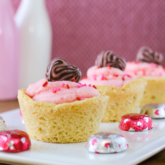 Side shot of three cookie cups in a row on a white plate with chocolate hearts scattered around.