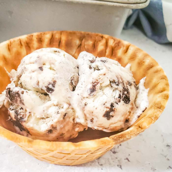 Side close up shot of ice cream in a waffle cone bowl on a white marble surface with a metal pan in 