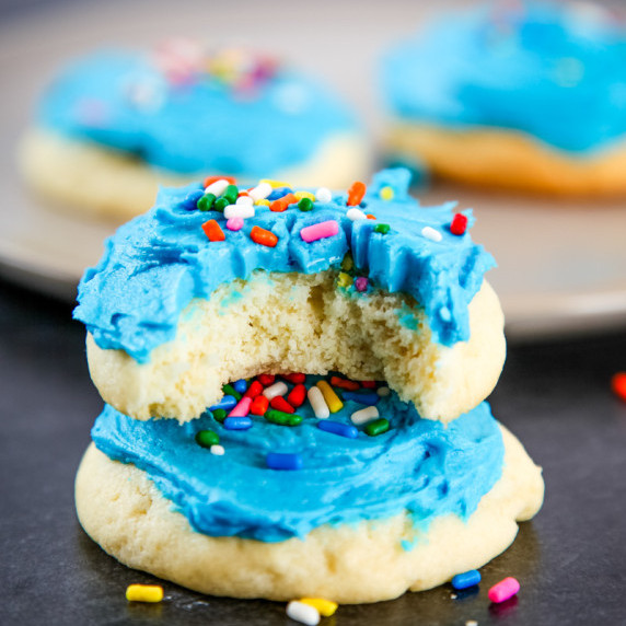 two soft sugar cookies with blue frosting and rainbow sprinkles. 