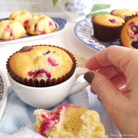 Close shot of a female hand reaching for a China cuo housing a cranberry muffin.