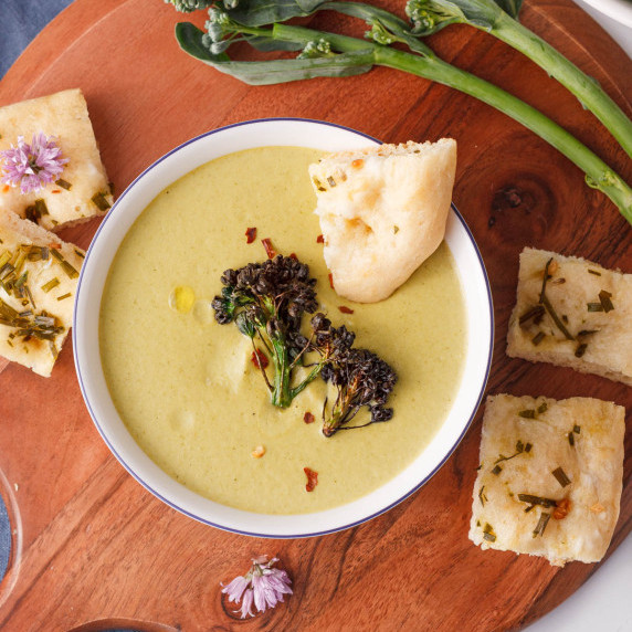 overhead image of cream of broccolini soup in bowl with bread and raw broccolini framing the bowl
