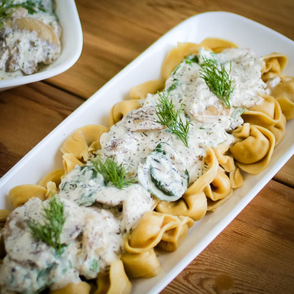 Side shot of mushroom sauce on top of tortellini pasta garnished with dill on a white plate.