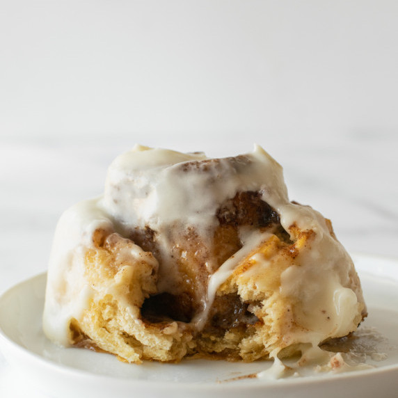 bite taken of a crescent roll cinnamon rolls on a white plate.