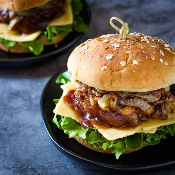 Side shot of barbecue burger with lettuce, cheese, caramelized onions, and a sesame bun.