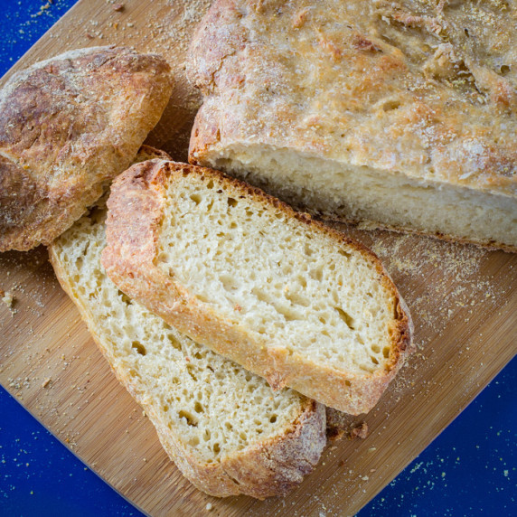 Overhead shot of half of the bread loaf with some slices on a wooden cutting board with a blue backg