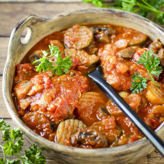 Side close up shot of chicken cacciatore in a large serving bowl with a black spoon inside.