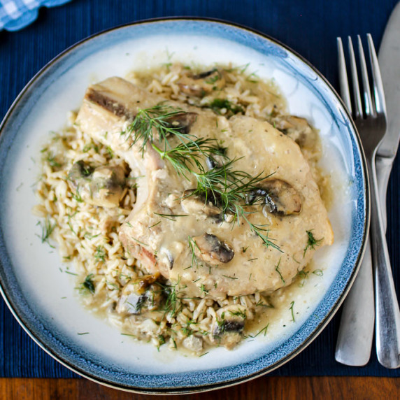 Side close up view of a pork chop on top of mushroom soup garnished with herbs on a white plate.