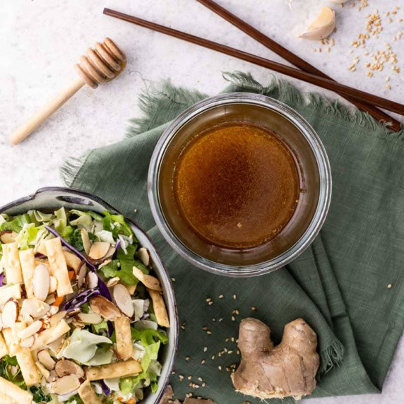 Overhead of a glass jar with homemade sesame ginger dressing alongside an asian-inspired salad.