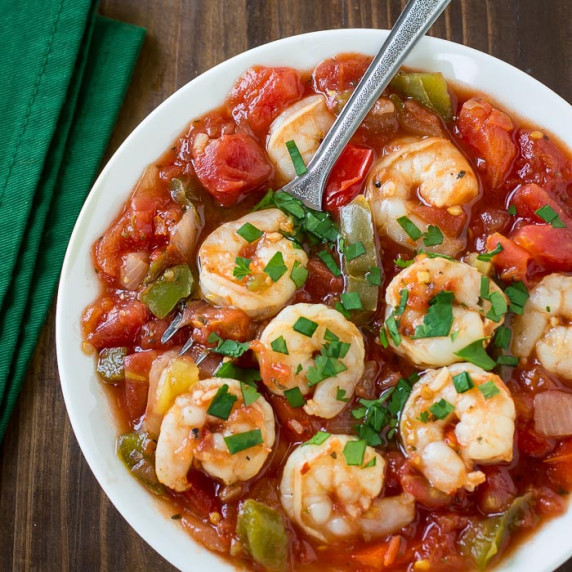 Side shot shrimp stew garnished with herbs in a white bowl with a fork on the side.