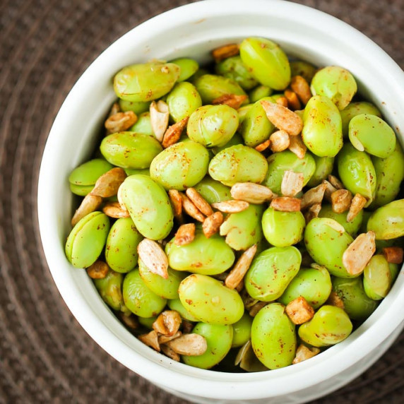 Close up overhead shot of chipotle edamame in a white bowl on a brown surface.