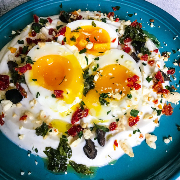 Jammy eggs on top of Greek yogurt with sun-dried tomatoes, black olives, feta, and parsley. 