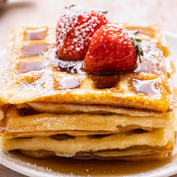 A stack of waffles with syrup and strawberries.
