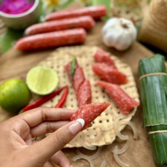 Hand holding a piece of som moo, fermented pork sausage.