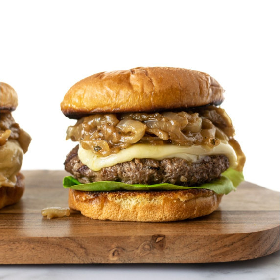 french onion burger topped with onions and melted cheese on a wood cutting board.