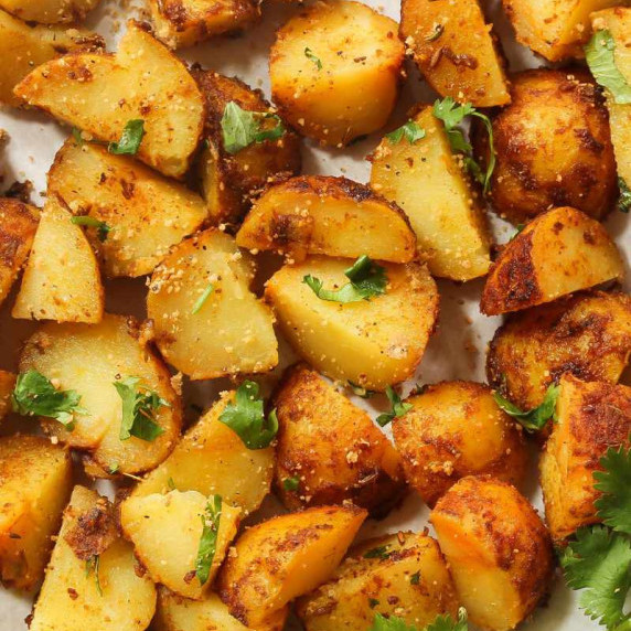 Close birdseye view of garlic roasted potatoes on a sheet pan with chopped parsley garnish.