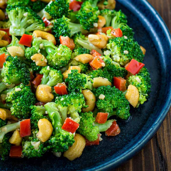 Side close up view of garlic butter broccoli in a blue bowl on a wooden surface.