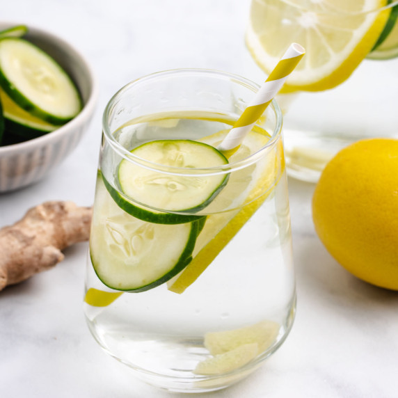  A glass of water with lemon, cucumber, and ginger slices with a straw.