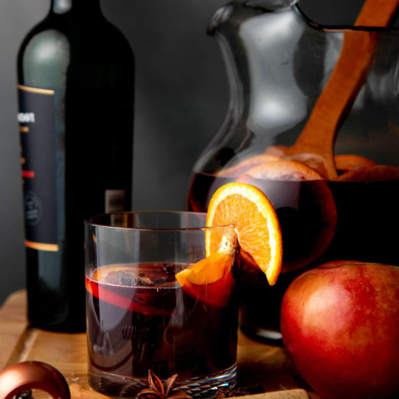 A glass of apple cider sangria garnished with an orange slice stands in front of pitcher of sangria.