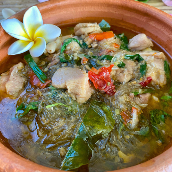 Glass noodles with chicken and chilies plus a white flower in a clay bowl.