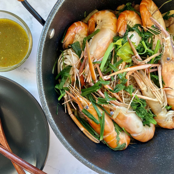 Goong ob woonsen (glass noodle with prawns) in a cooking pot with a sauce and a part of a black dish