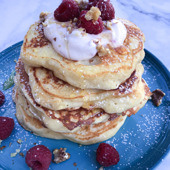 A stack of fluffy Greek yogurt pancakes topped with Greek yogurt, raspberries, and honey.
