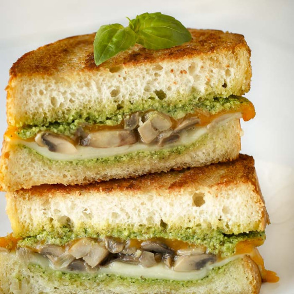 Side shot of two halves of grilled cheese mushroom sandwich garnished with basil.