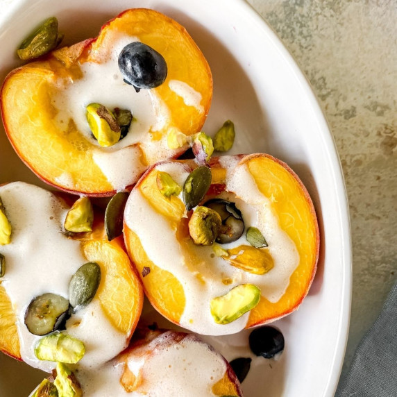 peaches in a white dish surrounded by a blue cloth, fruit and spoons.