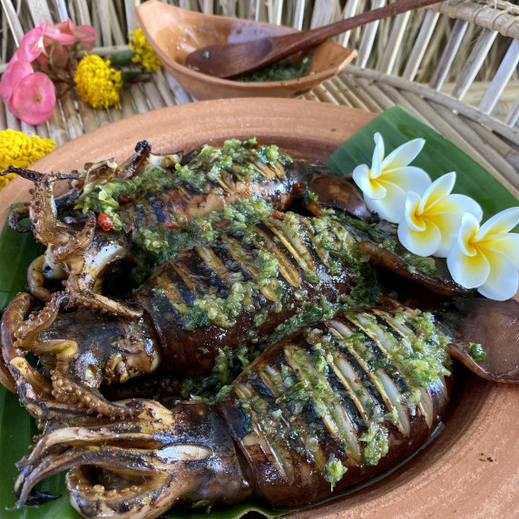 3 Thai grilled squid in a clay dish, topped with nam jim seafood, a green dipping sauce.