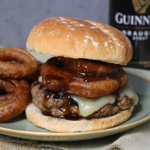 A juicy burger topped with cheddar cheese, onion rings, and Guinness glaze on a potato bun