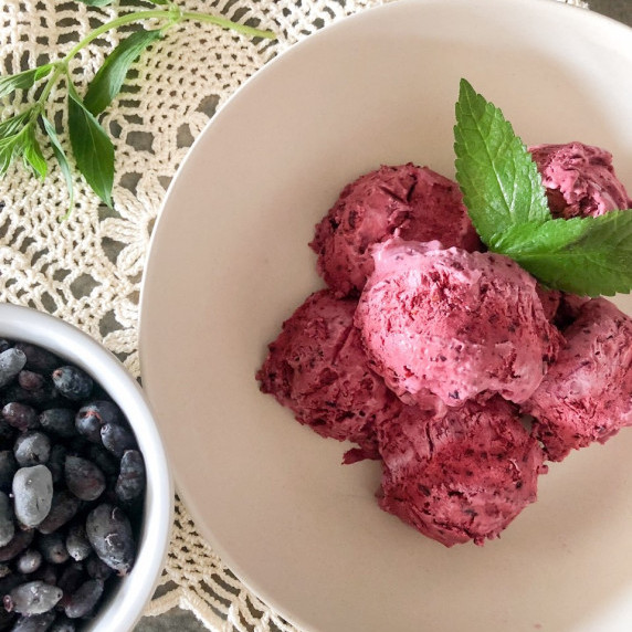 Scoops of haskap no-churn ice cream in a white bowl with haskap berries in a white dish beside it