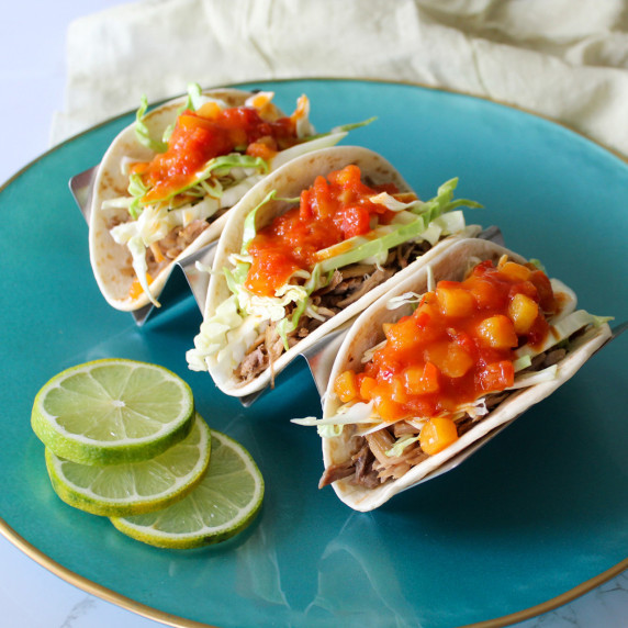 Three pulled pork tacos topped with cabbage and mango salsa served with lime wheels