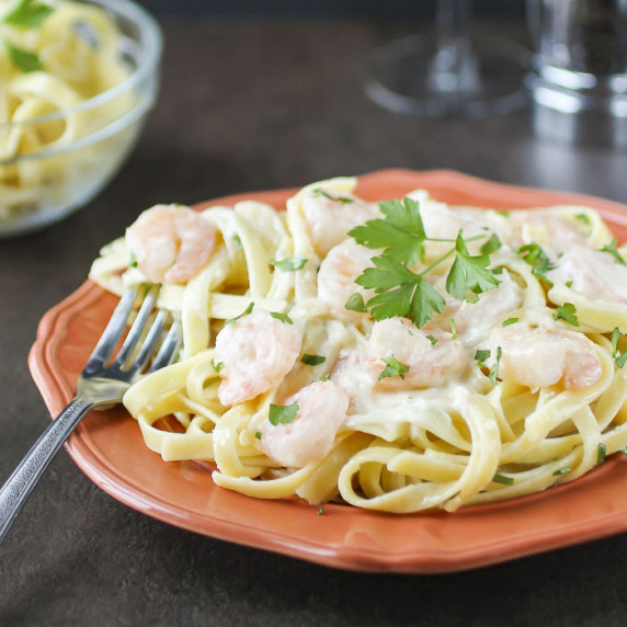 Side close up shot of shrimp fettuccine alfredo garnished with fresh parsley on an orange plate.