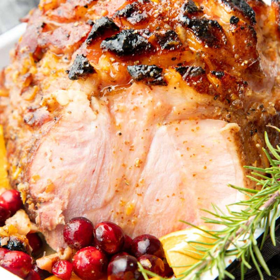 Sliced Christmas ham with orange bourbon glaze dripping down sits with cranberries and orange slices