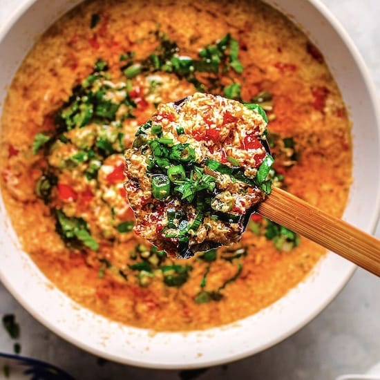Tomato egg drop soup with chives in a white bowl with a wooden spoon