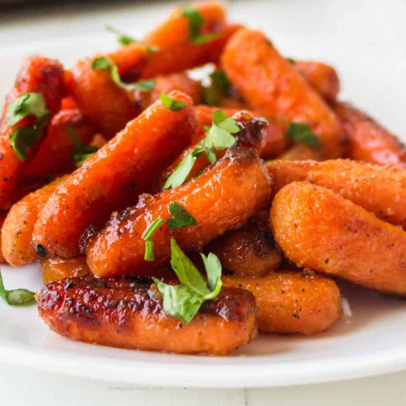 Close up side vide of glazed baby carrots piled on a plate.