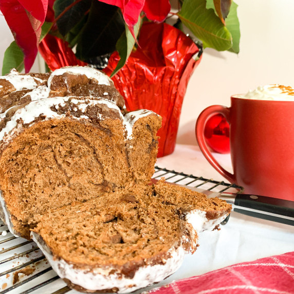 Sliced open hot chocolate babka with marshmallow glaze with a cup of cocoa behind