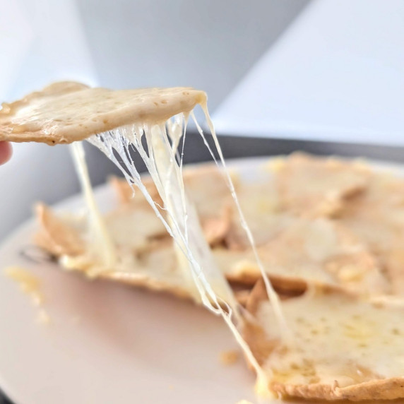 A microwave nacho being picked up with satisfying cheese pull