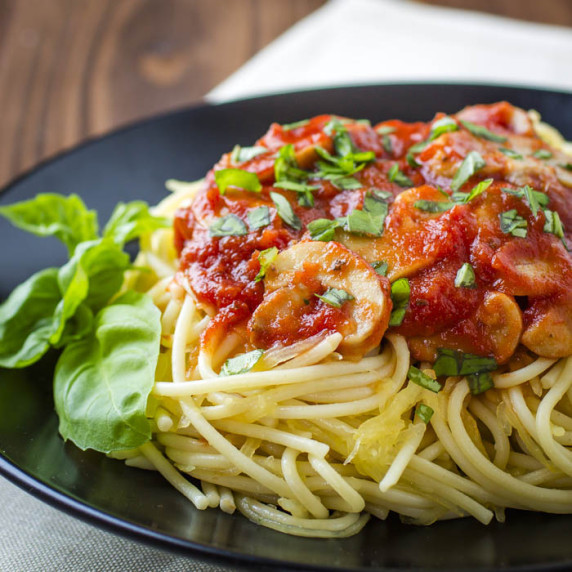 Side angled shot of pasta with a red mushroom sauce garnished with fresh basil on a black plate.